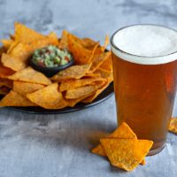 Glass of light beer on white stone background. Cold alcohol drink and snacks are prepared for a big friend's party. Concept of drinks, fun, food, celebrating, meeting, oktoberfest.